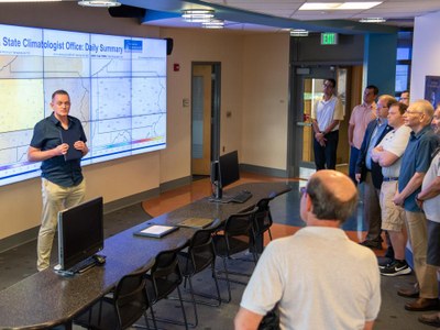 Group gathers in the Joel N. Myers Weather Center in front of the electronic map wall for WMO to honor Penn State Meteorology and Atmospheric Science for 130 years of weather observations.