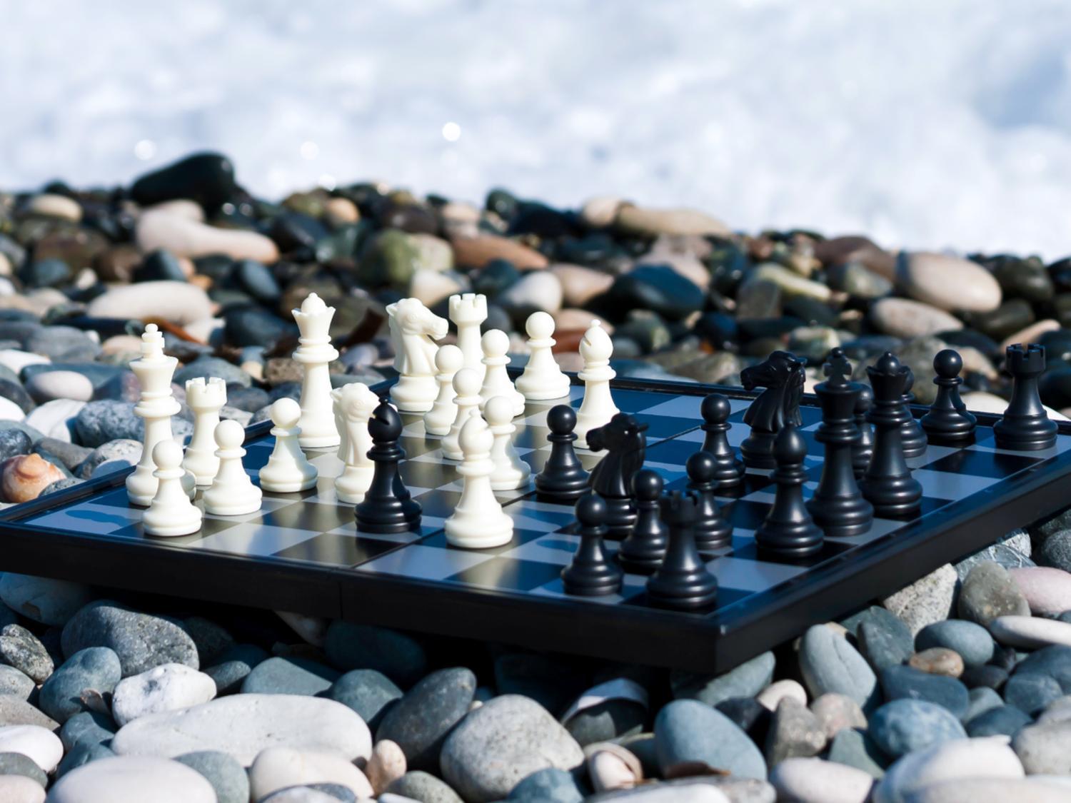 Chess board with black and white chess pieces on top pebbles from the ocean.